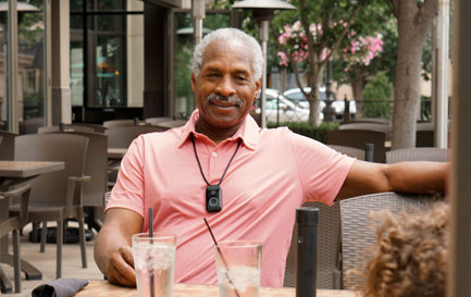 Sitting-outdoors-web Smiling senior man wearing a medical alert device at an outdoor restaurant